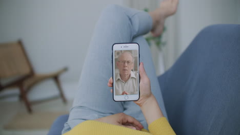 Over-shoulder-view-of-young-woman-daughter-video-calling-old-parent-father-or-mature-friend-using-conference-chat-online-application-on-mobile-phone-screen-at-home-office.-Family-videocall-concept